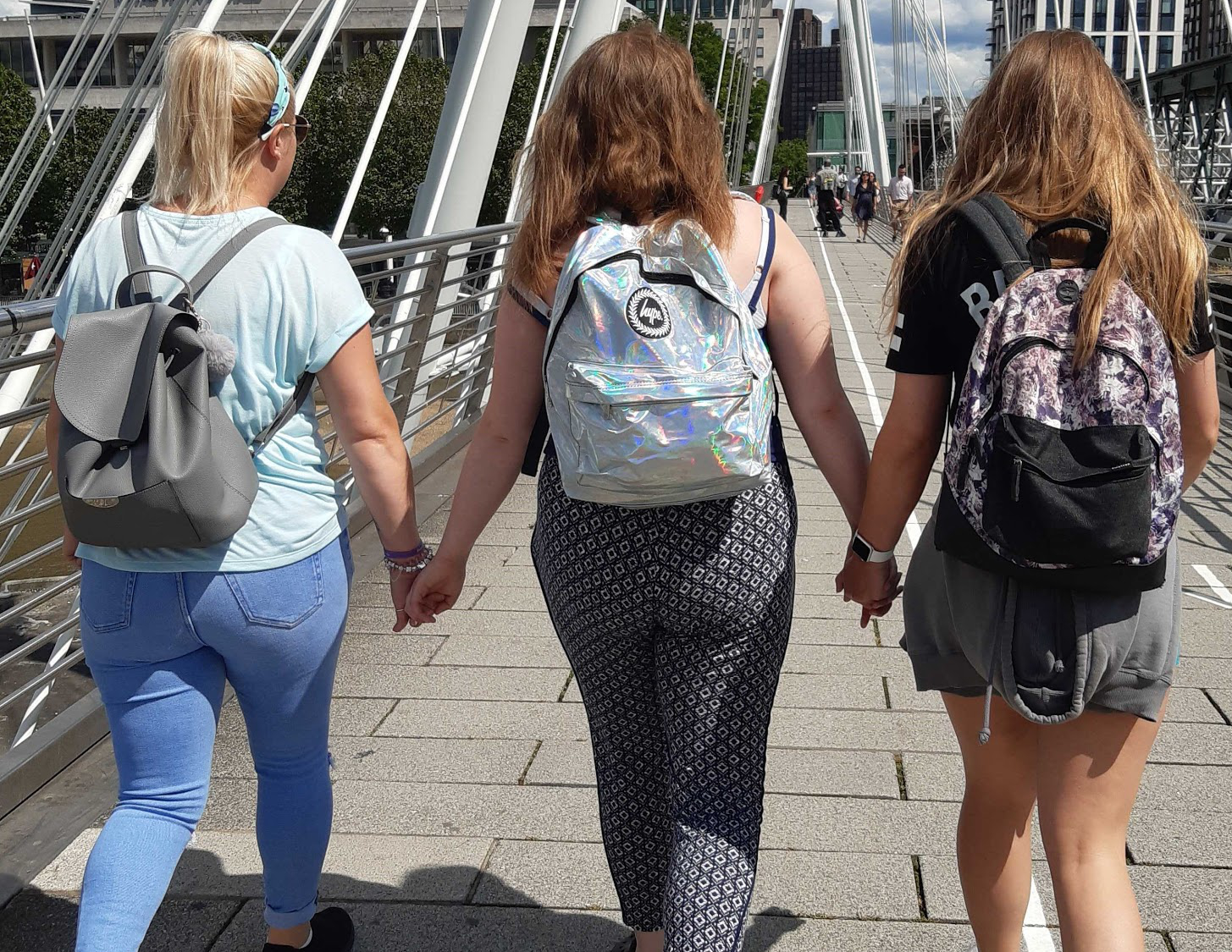 Three young women holding hands and walking across a bridge